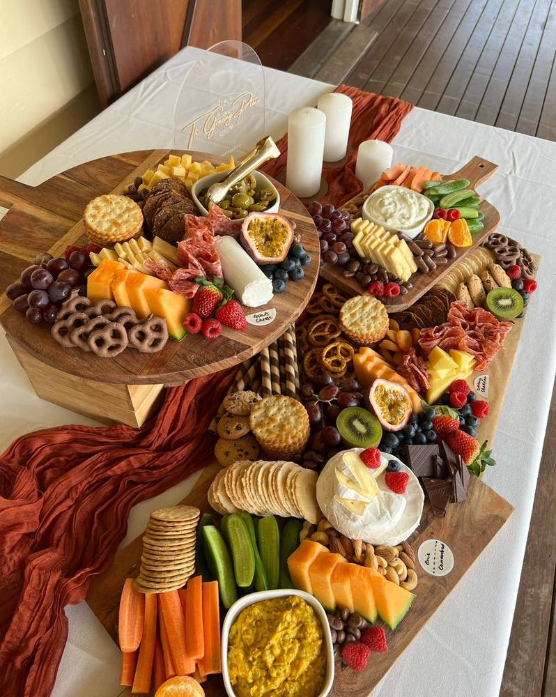Baby shower grazing on round timber boards, with a rust table runner and white candles