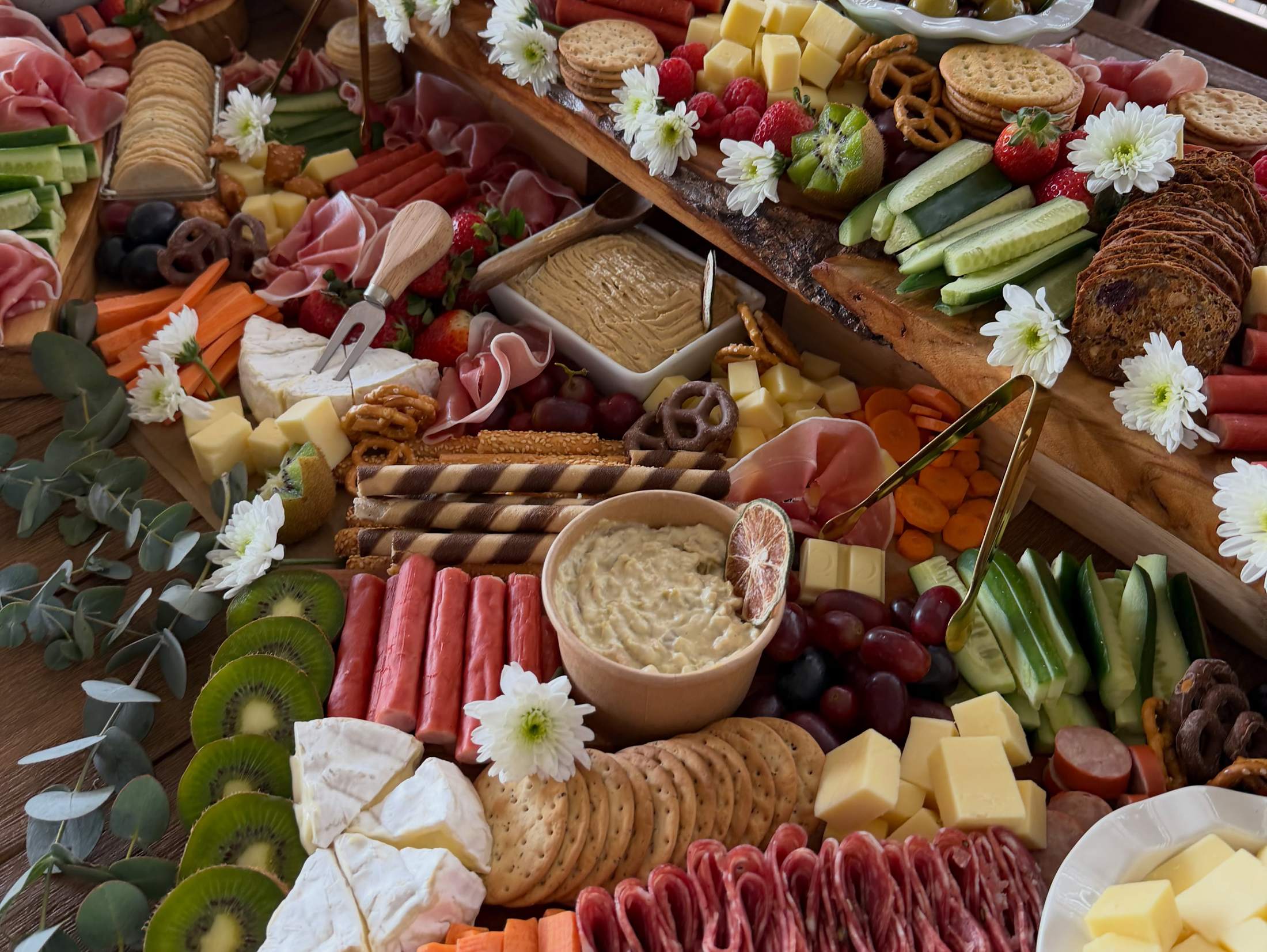 Close-up of cheeses, salami, kiwi fruit, dips and white daisies