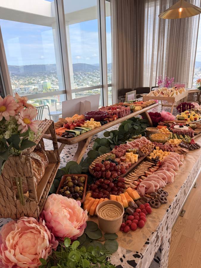 Long grazing table with pink peonies beside floor-to-ceiling windows